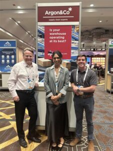 Three people at a booth at a conference standing and smiling at camera