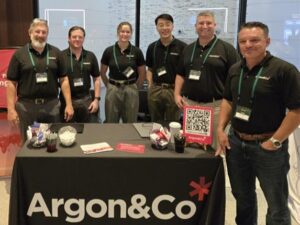 L-R Greg Colabello, Rob Achtzehn, Sophia Sassoli, Frank Tsang, Rich Cammisa and Chris Keller lined up behind a table with the Argon & Co logo on it