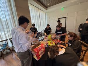 People standing around a round table putting things in plastic bags for kits for a children's hospital with Argon & Co shirts on